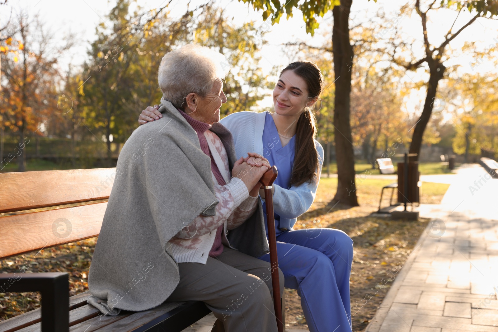 Photo of Elderly woman with walking cane and her caregiver in park