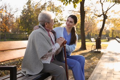 Photo of Elderly woman with walking cane and her caregiver in park