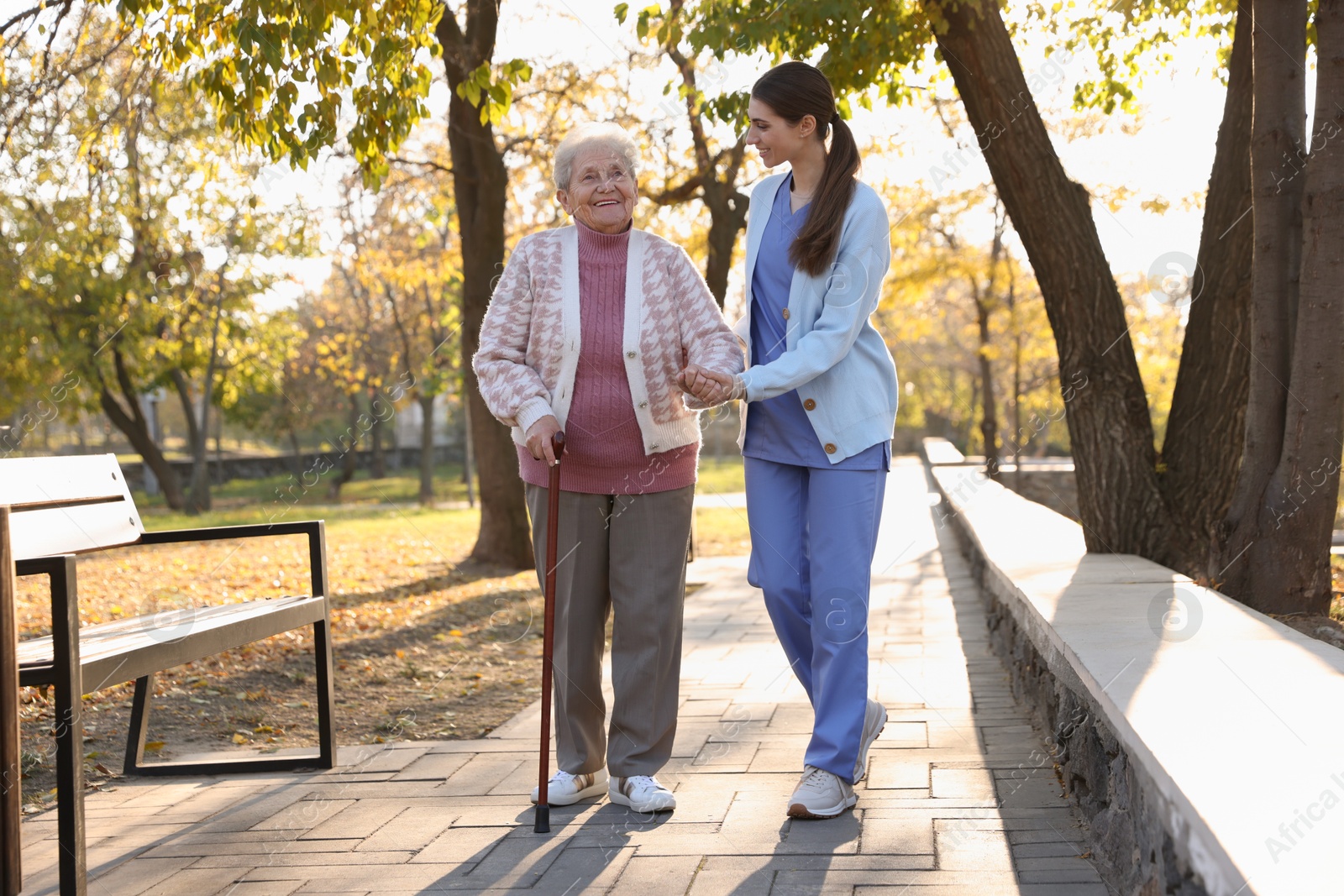 Photo of Elderly woman with walking cane and her caregiver in park