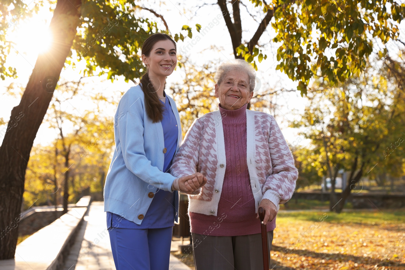 Photo of Elderly woman with walking cane and her caregiver in park