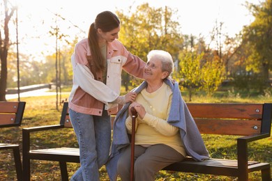 Photo of Elderly woman with walking cane and her caregiver in park