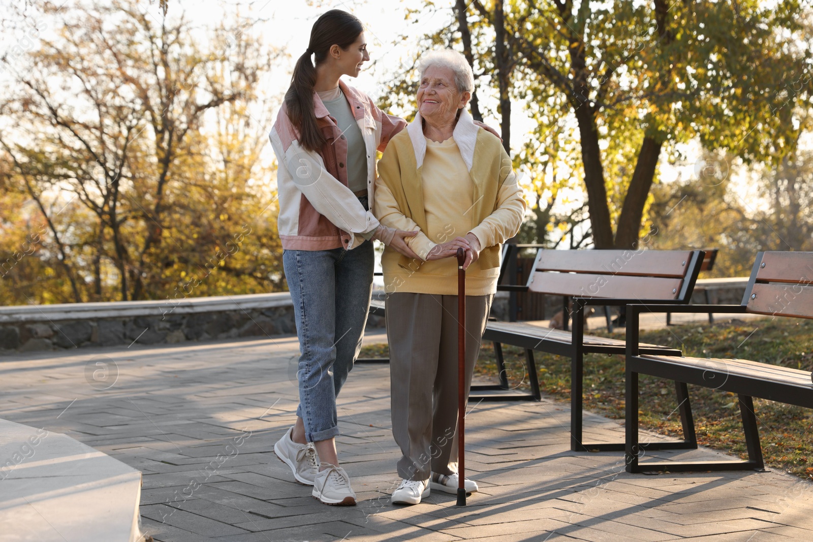 Photo of Elderly woman with walking cane and her caregiver in park