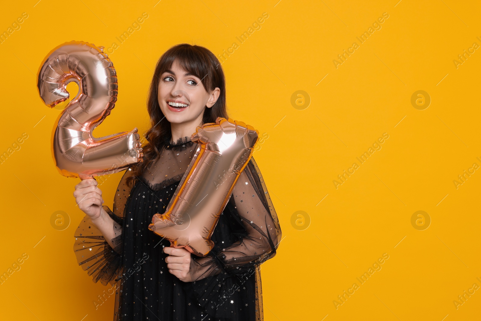 Photo of Coming of age party - 21st birthday. Young woman holding number shaped balloons on yellow background, space for text