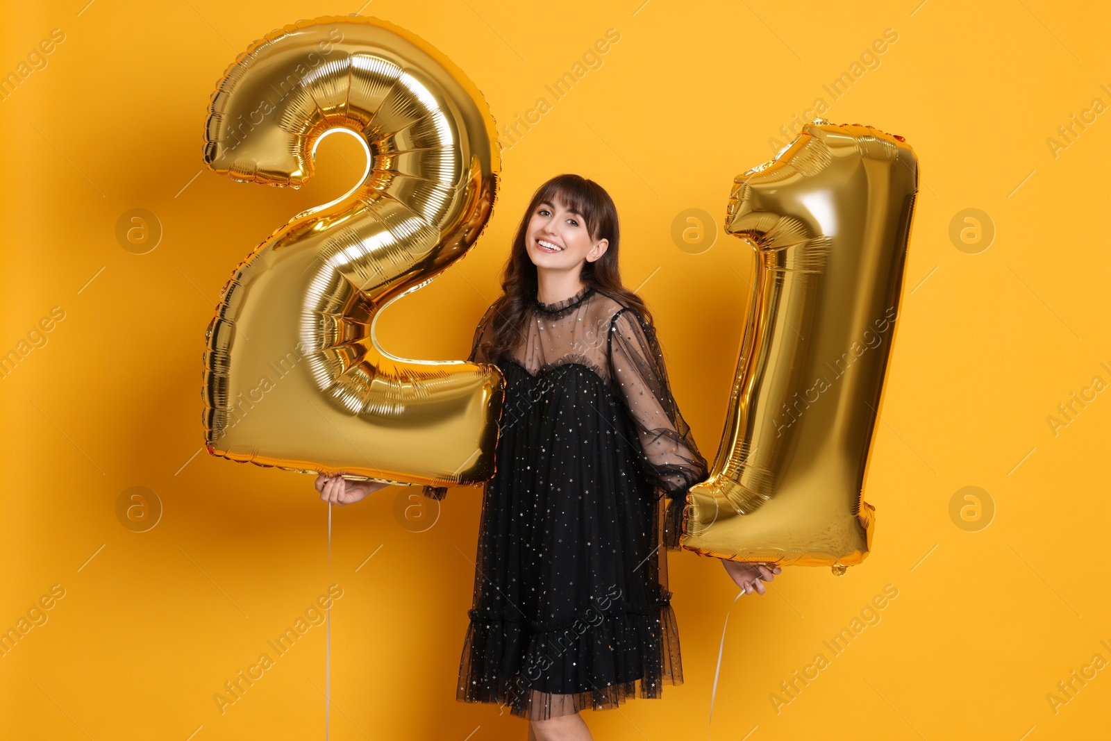 Photo of Coming of age party - 21st birthday. Young woman holding number shaped balloons on yellow background