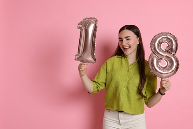 Photo of Coming of age party - 18th birthday. Happy young woman with number shaped balloons on pink background, space for text