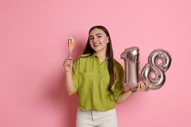 Photo of Coming of age party - 18th birthday. Happy young woman with number shaped balloons and glass of sparkling wine on pink background