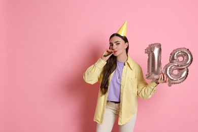 Photo of Coming of age party - 18th birthday. Happy young woman with number shaped balloons, hat and blower on pink background, space for text