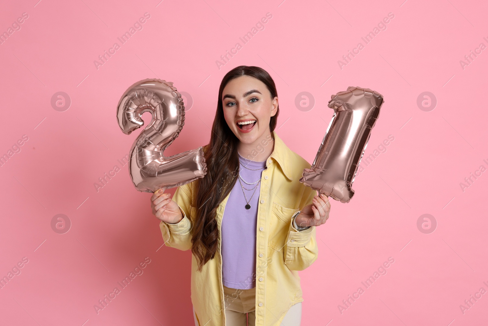 Photo of Coming of age party - 21st birthday. Happy young woman with number shaped balloons on pink background