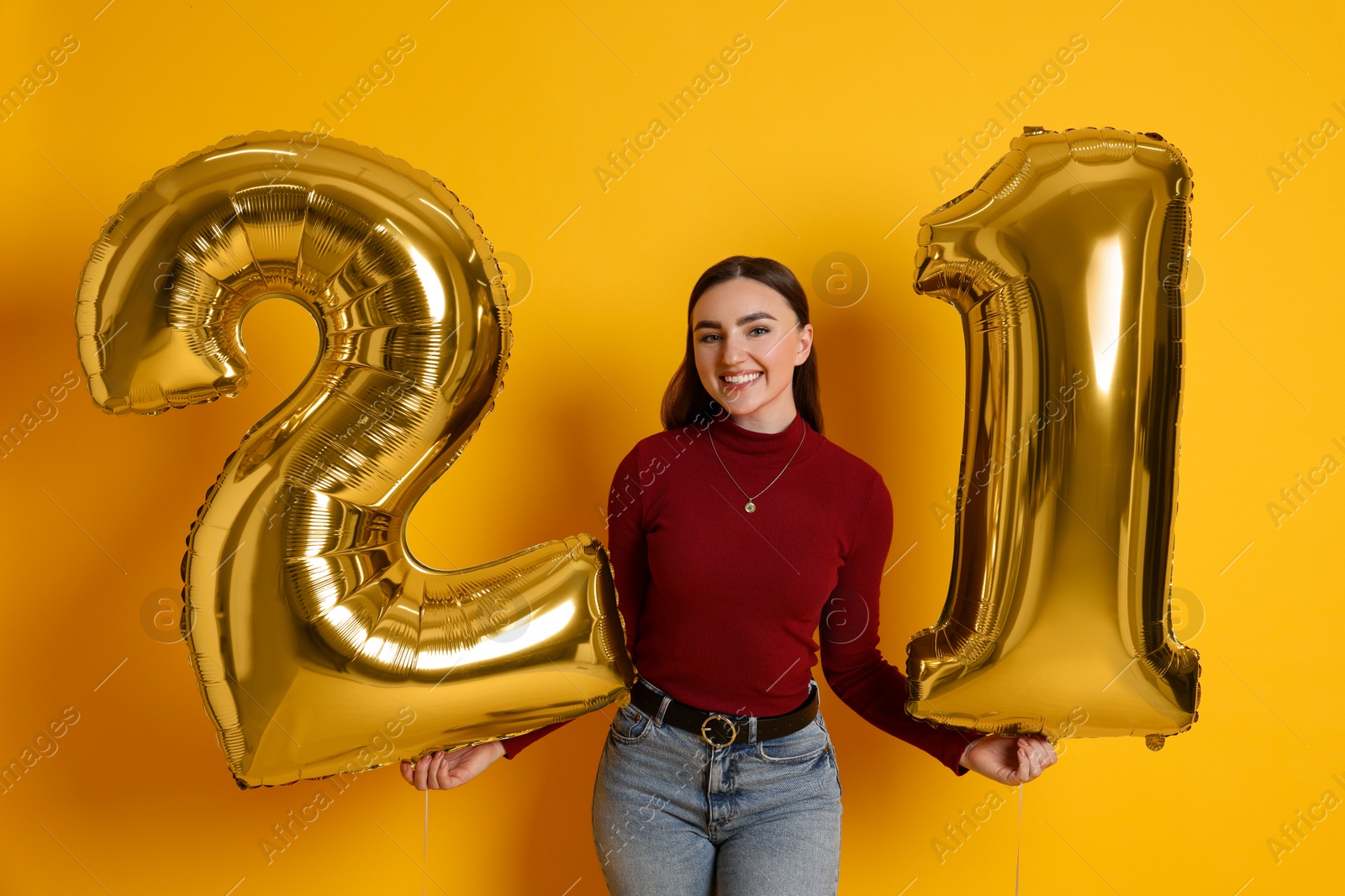 Photo of Coming of age party - 21st birthday. Happy young woman with number shaped balloons on yellow background