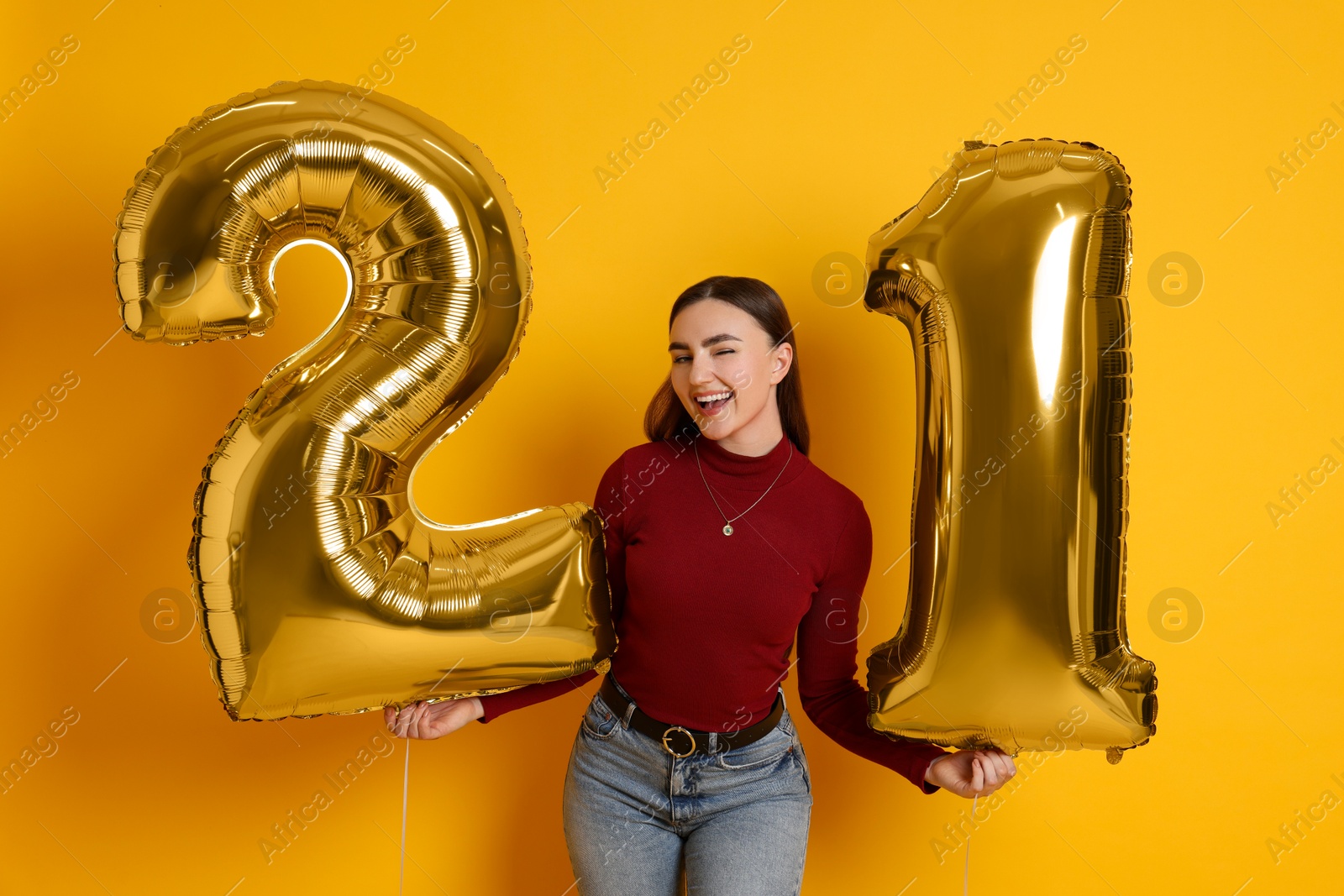 Photo of Coming of age party - 21st birthday. Happy young woman with number shaped balloons on yellow background