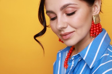 Photo of Young woman wearing stylish earrings and necklace on orange background, closeup. Space for text