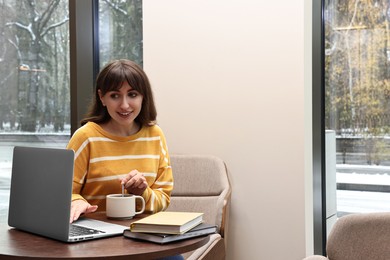 Photo of Smiling woman with laptop having coffee break at table in cafe. Space for text