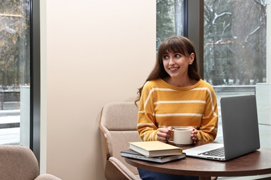 Photo of Smiling woman with laptop having coffee break at table in cafe. Space for text