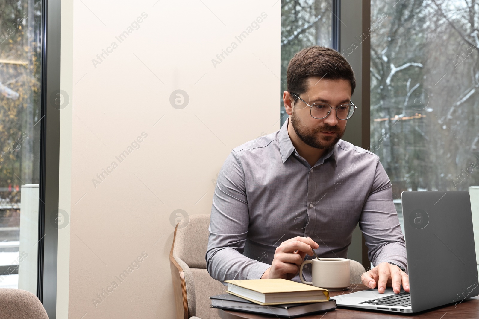 Photo of Businessman with laptop having coffee break at wooden table in cafe. Space for text