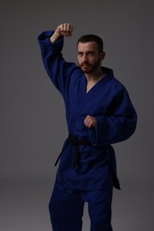 Photo of Man in uniform practicing karate on grey background