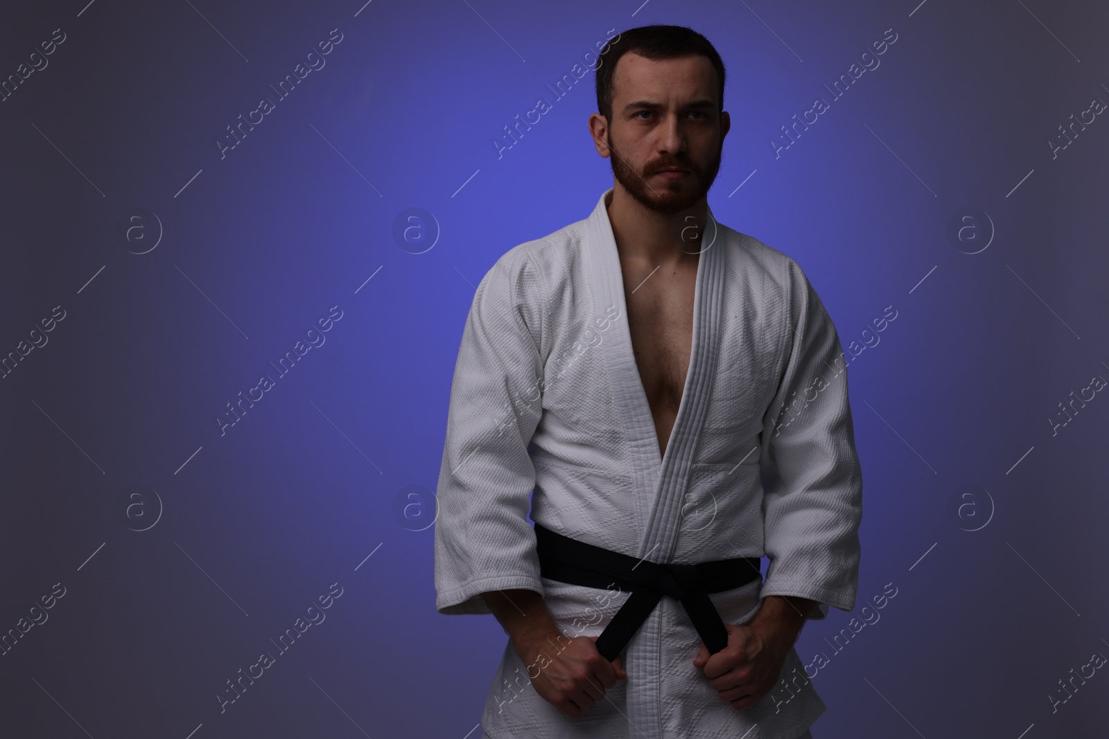 Photo of Karate fighter in uniform on dark purple background. Space for text