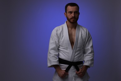 Photo of Karate fighter in uniform on dark purple background. Space for text