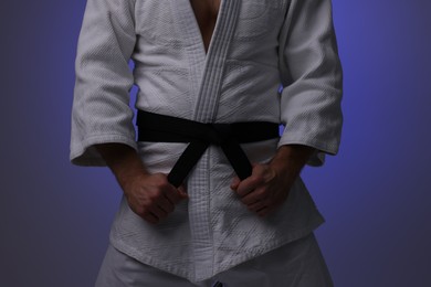 Photo of Karate fighter in uniform on dark purple background, closeup