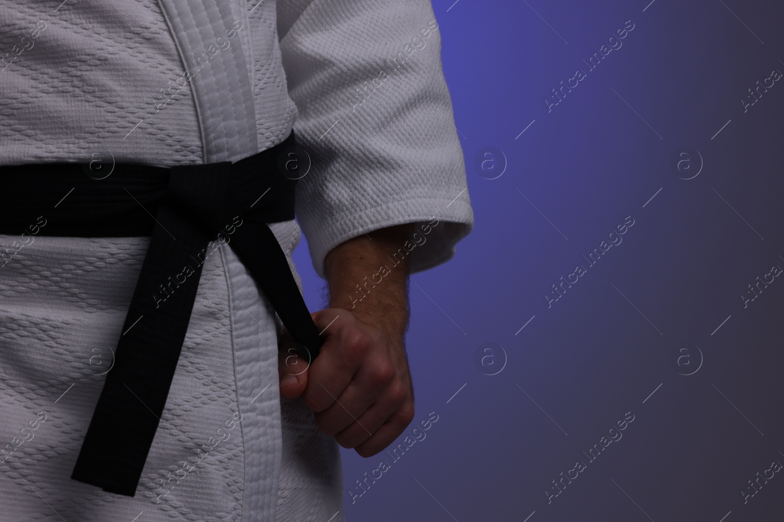 Photo of Karate fighter in uniform on dark purple background, closeup. Space for text