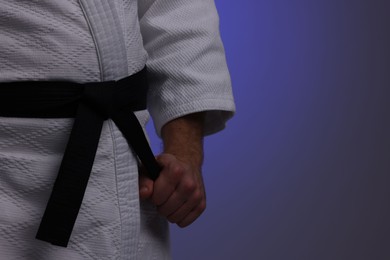 Photo of Karate fighter in uniform on dark purple background, closeup. Space for text