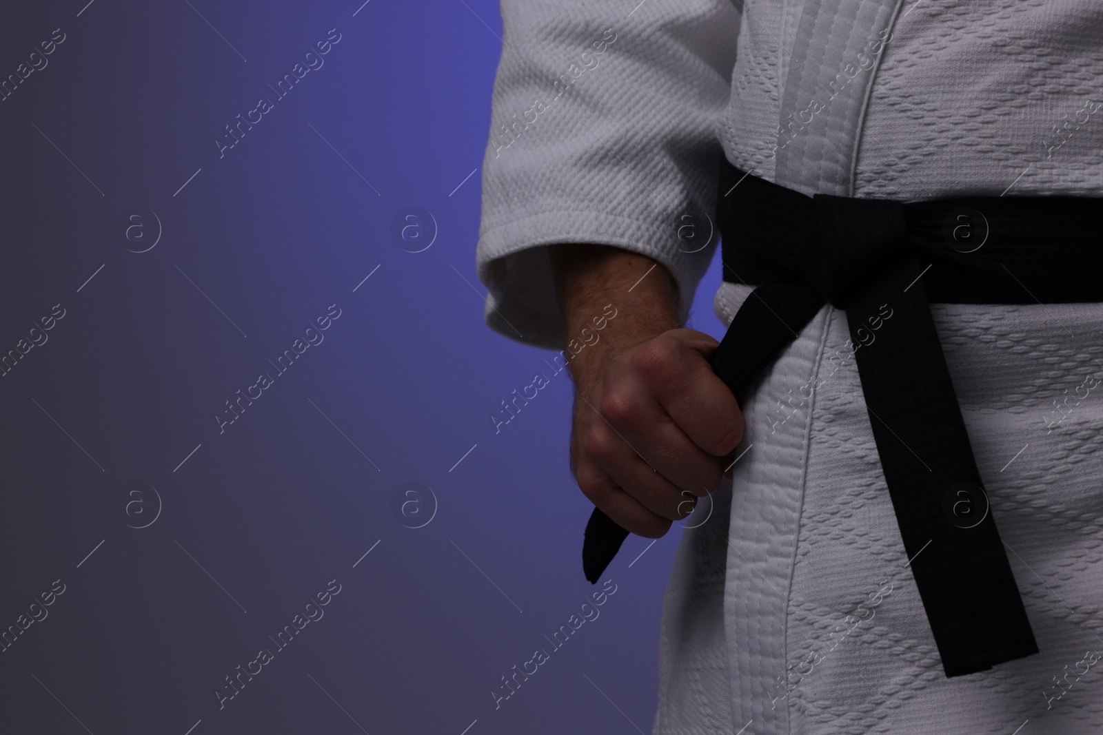 Photo of Karate fighter in uniform on dark purple background, closeup. Space for text