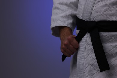 Photo of Karate fighter in uniform on dark purple background, closeup. Space for text