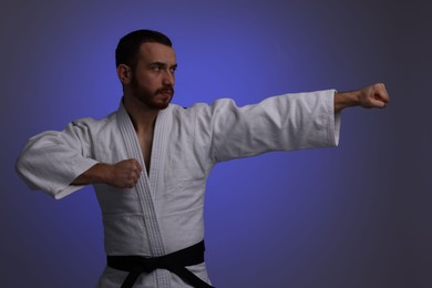 Photo of Man in uniform practicing karate on dark purple background