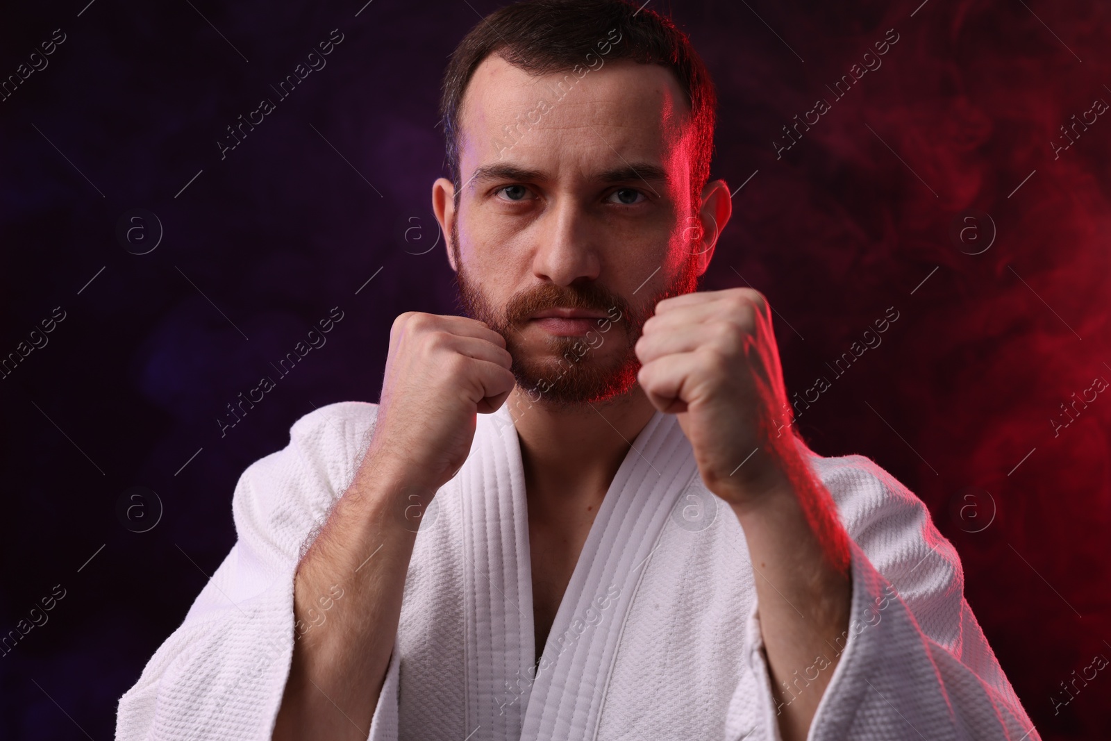 Photo of Karate fighter in color lights and smoke against black background