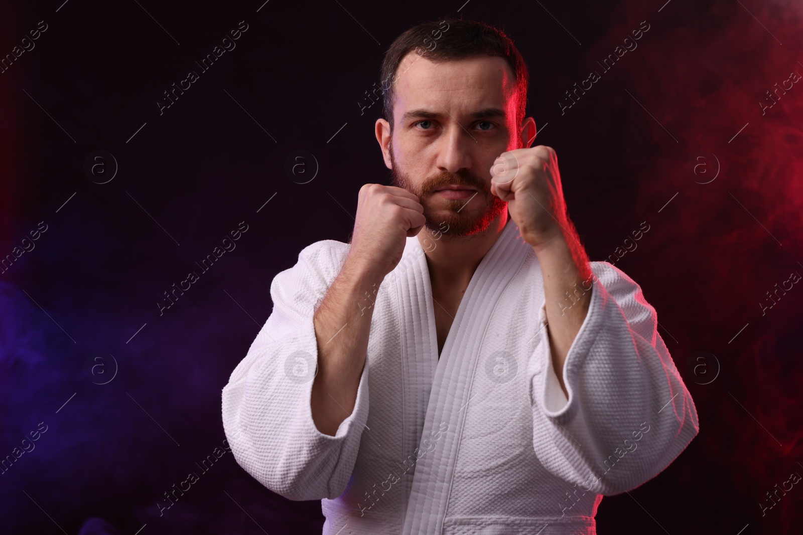 Photo of Karate fighter in color lights and smoke against black background. Space for text