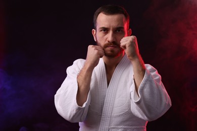 Karate fighter in color lights and smoke against black background. Space for text