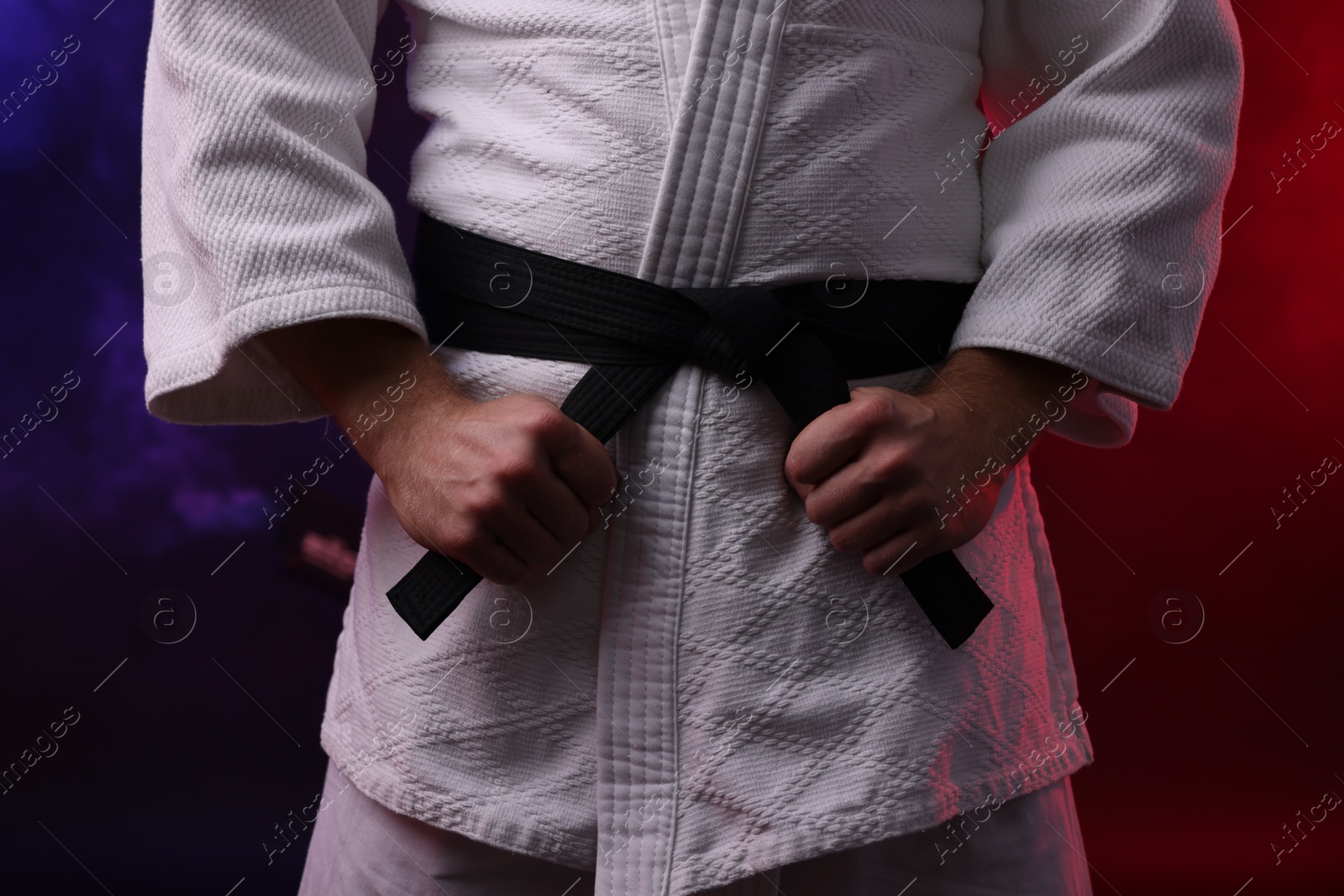 Photo of Karate fighter in kimono in color lights and smoke, closeup