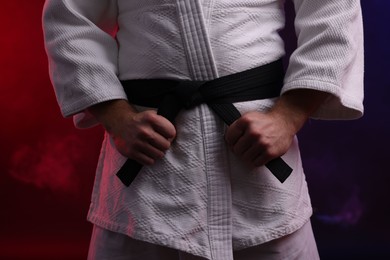 Photo of Karate fighter in kimono in color lights and smoke, closeup