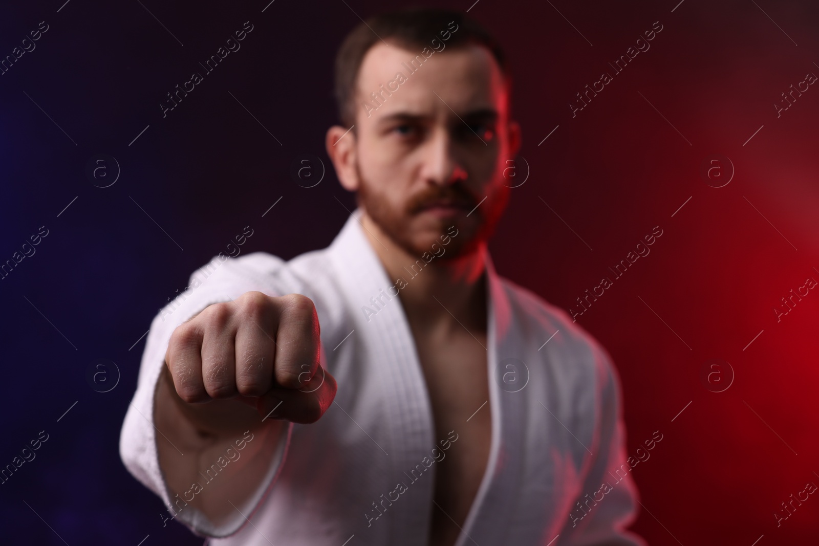 Photo of Man wearing uniform practicing karate in color lights and smoke, selective focus