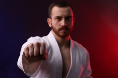 Photo of Man wearing uniform practicing karate in color lights and smoke, selective focus