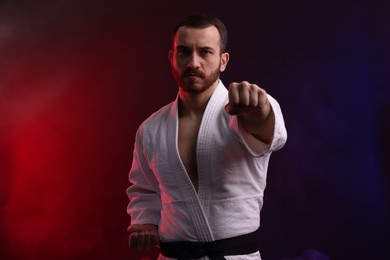 Photo of Man wearing uniform practicing karate in color lights and smoke