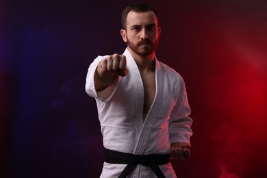 Photo of Man wearing uniform practicing karate in color lights and smoke