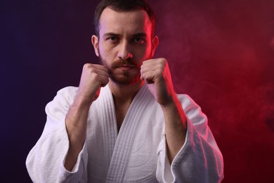 Photo of Karate fighter wearing uniform in color lights and smoke