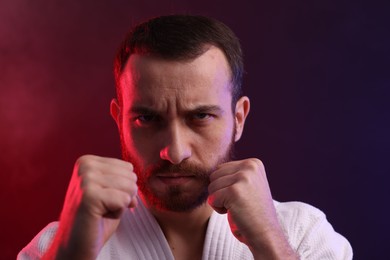 Photo of Karate fighter wearing uniform in color lights and smoke, closeup