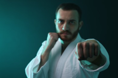 Photo of Man wearing uniform practicing karate in color lights, selective focus. Space for text