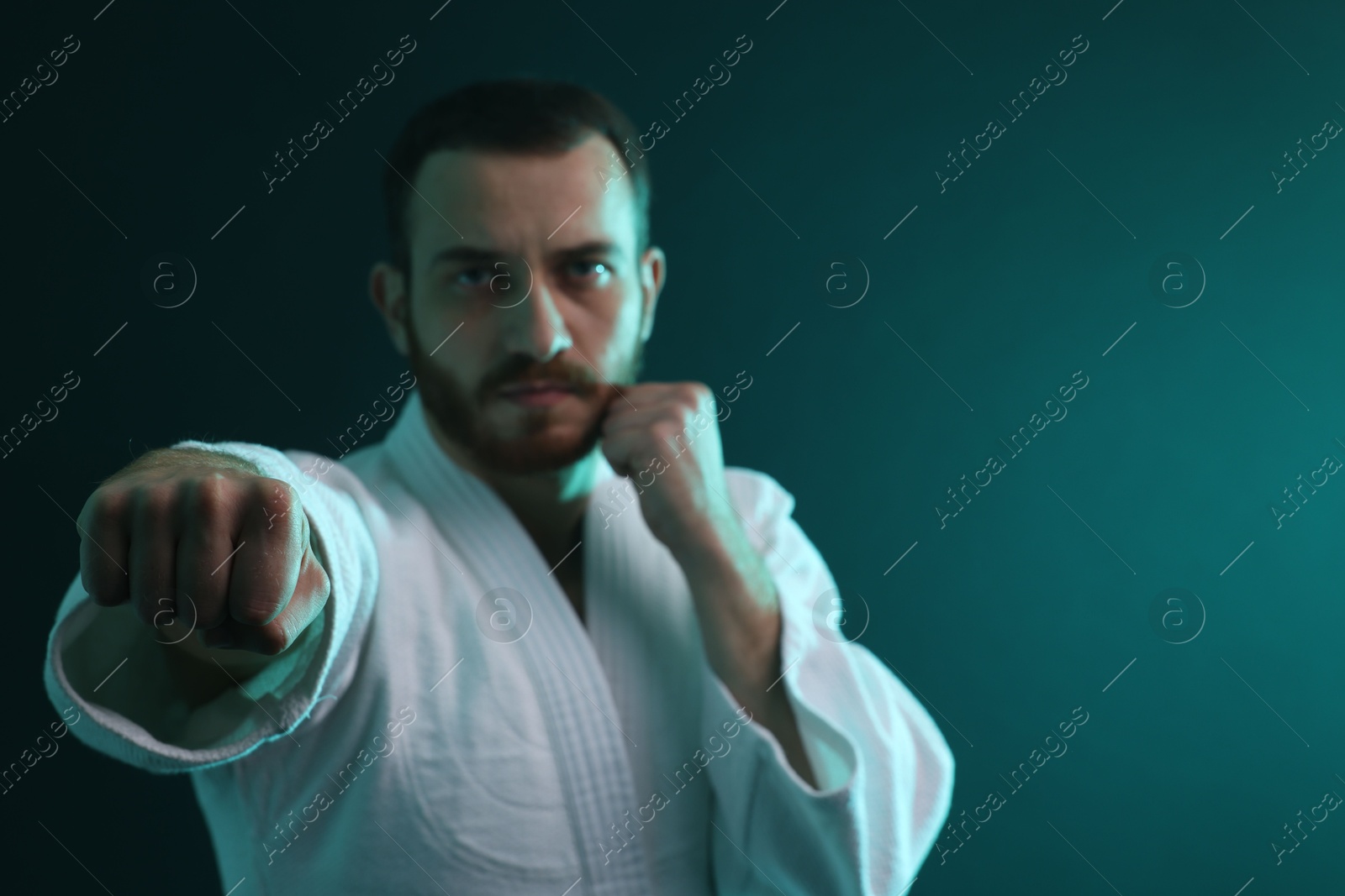 Photo of Man wearing uniform practicing karate in color lights, selective focus. Space for text