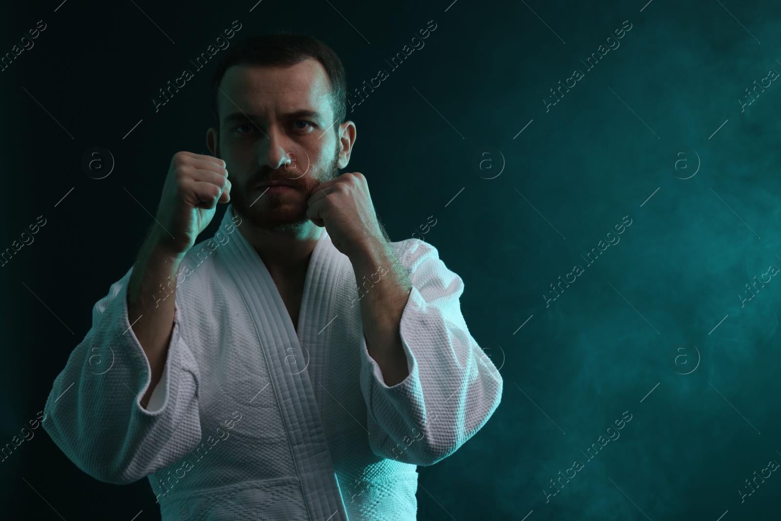 Photo of Man wearing uniform practicing karate in color lights and smoke. Space for text