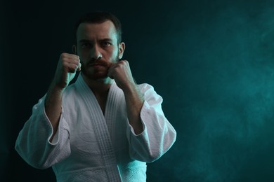 Photo of Man wearing uniform practicing karate in color lights and smoke. Space for text