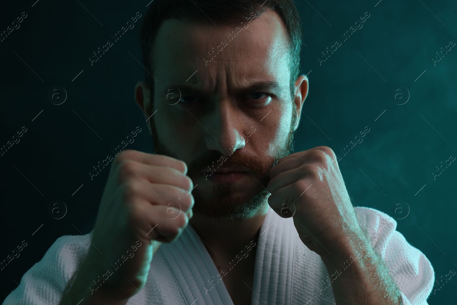 Photo of Karate fighter wearing uniform in color lights and smoke, closeup