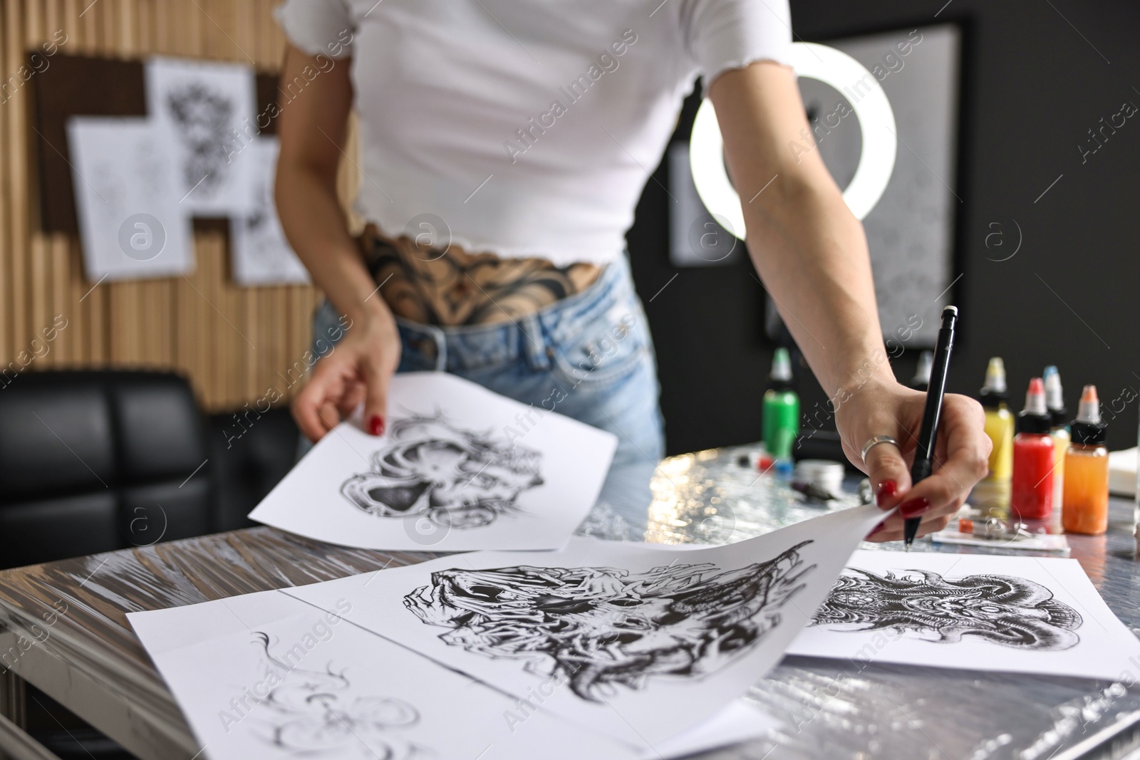 Photo of Tattoo artist working with sketches at table in salon, closeup