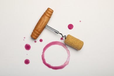 Photo of Corkscrew, cork and red wine stains on white background, top view