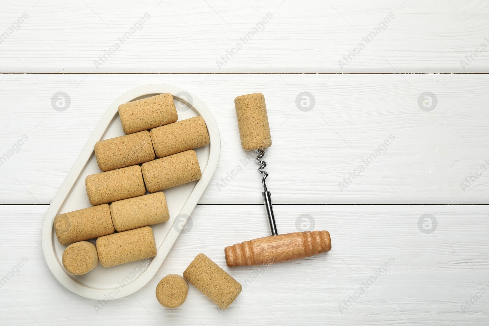 Photo of Corkscrew and corks on white wooden table, flat lay. Space for text