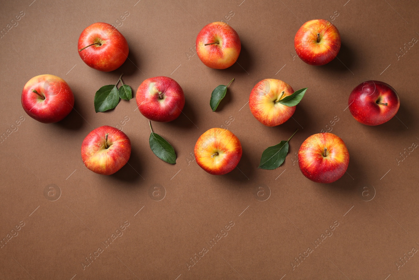 Photo of Ripe red apples and green leaves on brown background, flat lay