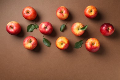 Ripe red apples and green leaves on brown background, flat lay