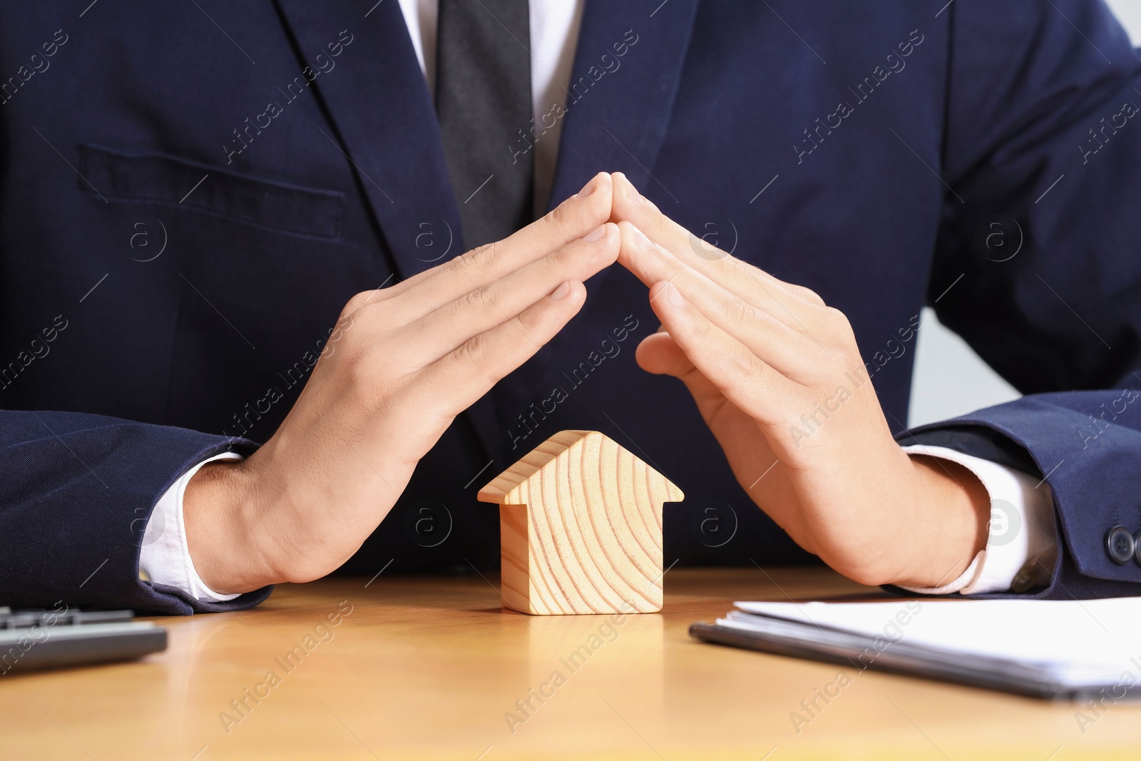 Photo of Property insurance. Real estate agent protecting house figure at table, closeup