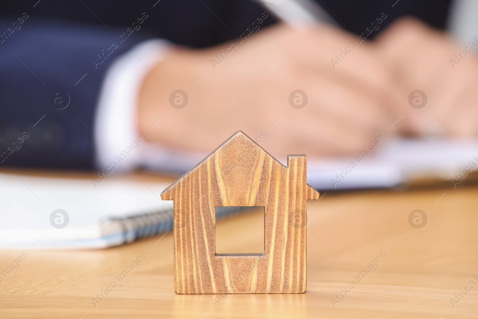 Photo of Property insurance. Real estate agent working at table indoors, focus on wooden house figure